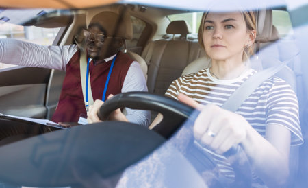 Driving school concept. A car instructor teaches a young woman how to drive. Teaching the rules of the road and driving a vehicleの写真素材