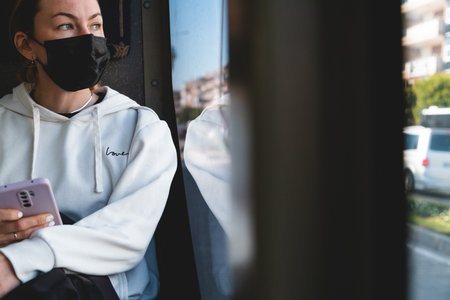 A yong woman in a protective medical mask sits near the window on the bus. Social distance and protection against covid-19 virus in public transport.の写真素材