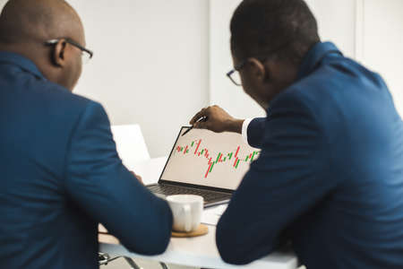 Two African American business partners are working on a laptop studying stock market charts and technical analysis. Training in investment and analysis of macroeconomic and financial indicatorsの写真素材