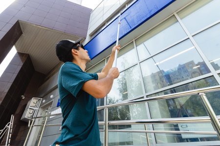 An employee of a professional cleaning service in overalls washes the glass of the windows of the facade of the building. Showcase cleaning for shops and businessesの写真素材
