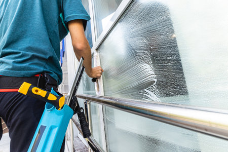 Male professional cleaning service worker in overalls cleans the windows and shop windows of a store with special equipmentの写真素材