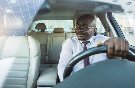 Portrait of a handsome African American businessman in a suit and glasses driving his new personal...