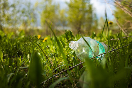 Abandoned garbage plastic and glass waste in nature among the grass. Environmental damage caused by...