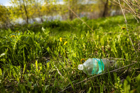 Abandoned garbage plastic and glass waste in nature among the grass. Environmental damage caused by...