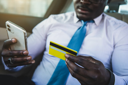 African American businessman makes online purchases from the phone while sitting in the back seat of the car and using a credit cardの写真素材