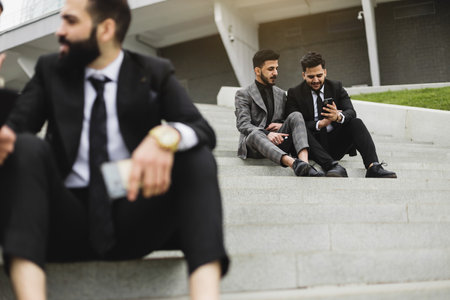 Business people outdoor meeting. A company of male businessmen in suits are sitting on the steps of the stairs. Working break. Discussion and conversation.の写真素材