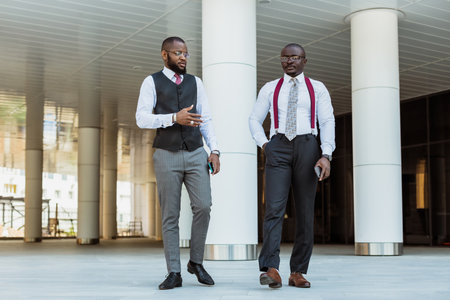 Portrait of two dark-skinned businessmen talking in the background of a modern building exterior. Friendly meeting outdoorsの写真素材