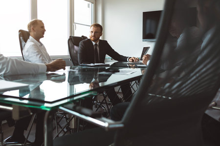 A group of company employees sits at a table in a meeting room. A team of young businessmen working and communicating together in an office. Corporate business team and manager in a meetingの写真素材