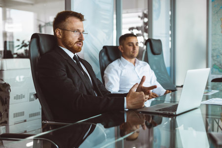 A group of company employees sits at a table in a meeting room. A team of young businessmen working and communicating together in an office. Corporate business team and manager in a meetingの写真素材