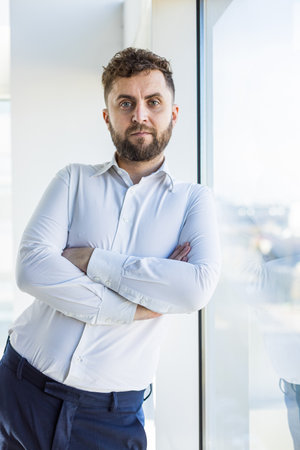Portrait of a business young successful man in a modern office standing by the window against the backdrop of the cityの写真素材