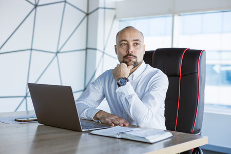 Portrait of a business young successful man in a modern office sitting at a tableの写真素材