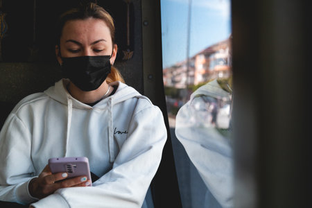 A yong woman in a protective medical mask sits near the window on the bus. Social distance and protection against covid-19 virus in public transport.の写真素材