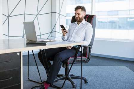Portrait of a business young successful man in a modern office sitting at a tableの写真素材