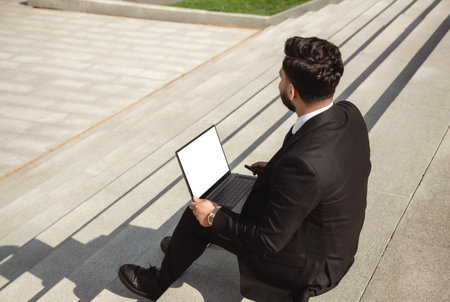 A man in a suit sits on the steps of a city staircase with a laptop. Working break. outdoors. business lifestyleの写真素材