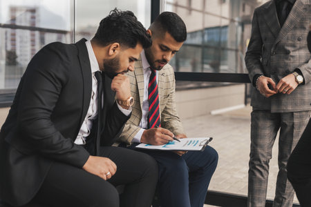 Business people outdoor meeting. Men in jackets discuss working moments together by brainstorming. Teamwork and partnership in business processesの写真素材
