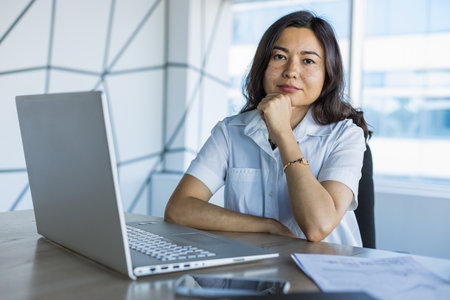 Portrait of a business young successful asian woman in a modern office sitting at a tableの写真素材