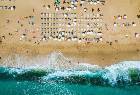 aerial shooting from a drone on a sandy beach with people sunbathing and relaxing. Flat view of the shore and turquoise waves of the surf and people bathingの写真素材