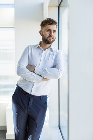 Portrait of a business young successful man in a modern office standing by the window against the backdrop of the cityの写真素材