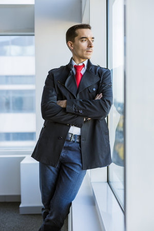 Portrait of a business young successful man in a modern office standing by the window against the backdrop of the cityの写真素材