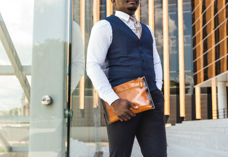 Portrait of handsome afro american businessman using phone in suit against modern building exterior. reflection in glassの写真素材