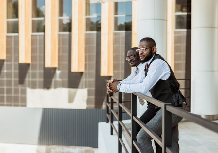 Portrait of two dark-skinned businessmen talking in the background of a modern building exterior. Friendly meeting outdoorsの写真素材