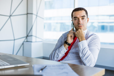 Portrait of a business young successful man in a modern office sitting at a tableの写真素材