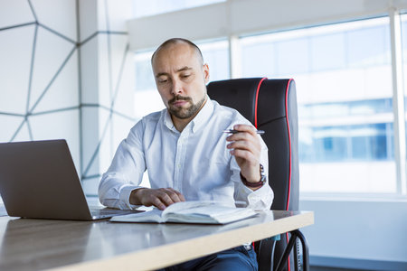 Portrait of a business young successful man in a modern office sitting at a tableの写真素材