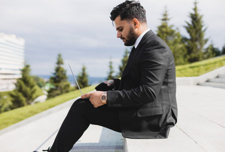 A man in a suit sits on the steps of a city staircase with a laptop. Working break. outdoors. business lifestyleの写真素材