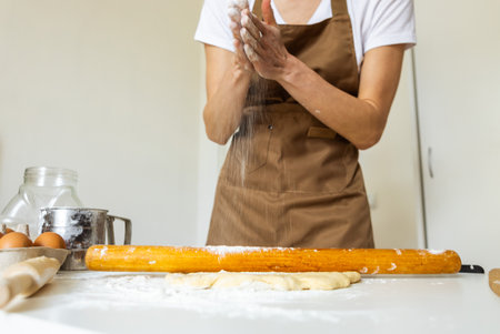 A woman in a special apron cooks at home. Rolling out and preparing dough for baking.の写真素材