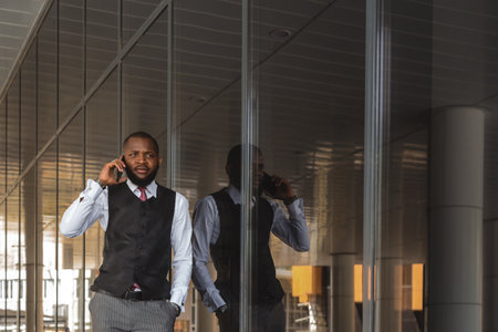 Portrait of handsome afro american businessman using phone in suit against modern building exteriorの写真素材