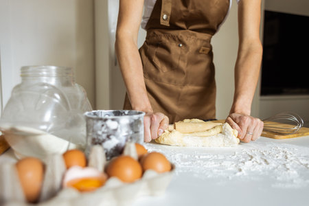 A woman in a special apron cooks at home. Rolling out and preparing dough for baking.の写真素材