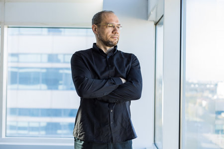 Portrait of a business young successful man in a modern office standing by the window against the backdrop of the cityの写真素材