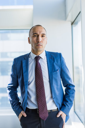 Portrait of a business young successful man in a modern office standing by the window against the backdrop of the cityの写真素材