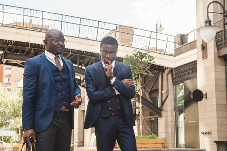 Two dark-skinned african american businessmen in suits with briefcases walk along the city streetの写真素材
