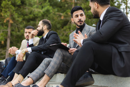 Business people outdoor meeting. A company of male businessmen in suits are sitting on the steps of the stairs. Working break. Teamwork and brainstorming. Successful teamworkの写真素材