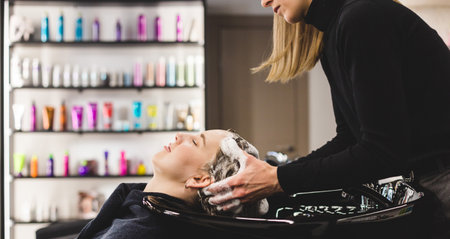 Master woman hairdresser washes hair of a girl with shampoo before styling in a beauty salon.の写真素材