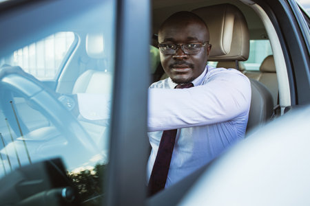 Portrait of a handsome African American businessman in a suit and glasses driving his new personal carの写真素材