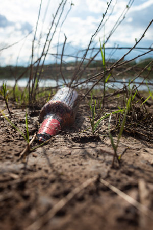Abandoned garbage in nature. Environmental damage caused by garbage pollution. Left glass bottle among the grass against the background of the riverの写真素材