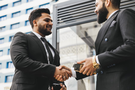 Business people outdoor meeting. Two men in suits hold out their hands to each other. A handshake is a mutual agreement. Greeting and interpersonal contactの写真素材