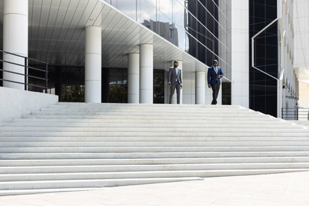 Business people walk down the stairs to a modern glass building. Work in a large company. Career growth and advancement. Increasing and improving skills. Salary increaseの写真素材