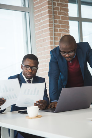 Two dark-skinned partners of an African American businessman in a meeting work on a laptop in the office. Affordable private courses and distance learning. New opportunities onlineの写真素材