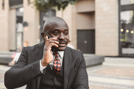 Portrait of black african american businessman in a suit with glasses and headphones stands against the background of city buildings outdoorsの写真素材