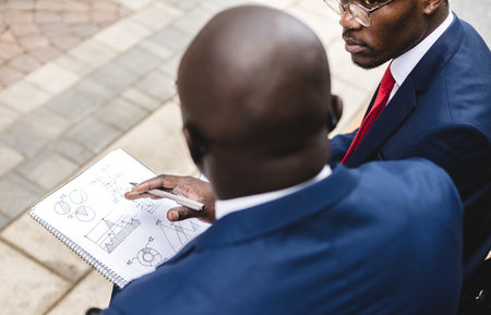 Friendly meeting of two dark-skinned African American businessman outdoors. Partners sit on a bench and discuss a joint projectの写真素材
