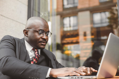 Portrait of black african american businessman in suits sits at a table in a summer cafe with a laptop outdoorsの写真素材