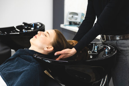 Master woman hairdresser gently washes the girls hair with shampoo and conditioner before styling in a beauty salon.の写真素材