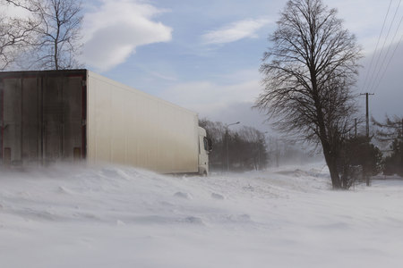 A large truck sneaks through snowdrifts on a dangerous road covered with snow. TIR fights the winter element. Difficulties in traffic during a snowstorm. The consequences of cold weather and waterの写真素材