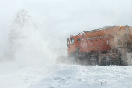 A large car with a plow clears the road from snow. Orange cargo special equipment is struggling with the elements in winter. Removing the effects of the snowstorm. Difficulties in traffic.Frozen waterの写真素材