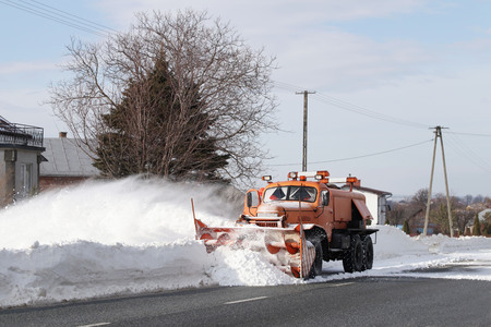 A large car with a plow clears the road from snow. Orange cargo special equipment is struggling with...