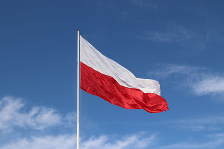 White-red horizontal flag on a flagpole developing in the wind against a blue sky with light clouds. Symbol of the Polish state.の写真素材