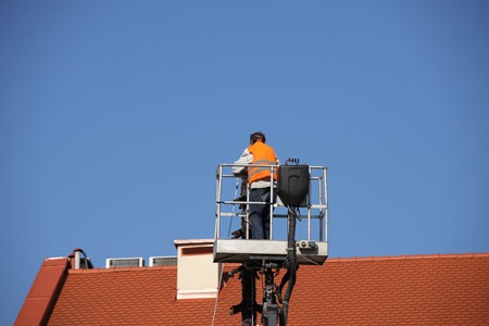 The worker in overalls works at height in a building mechanical lifting basket. Repair and...